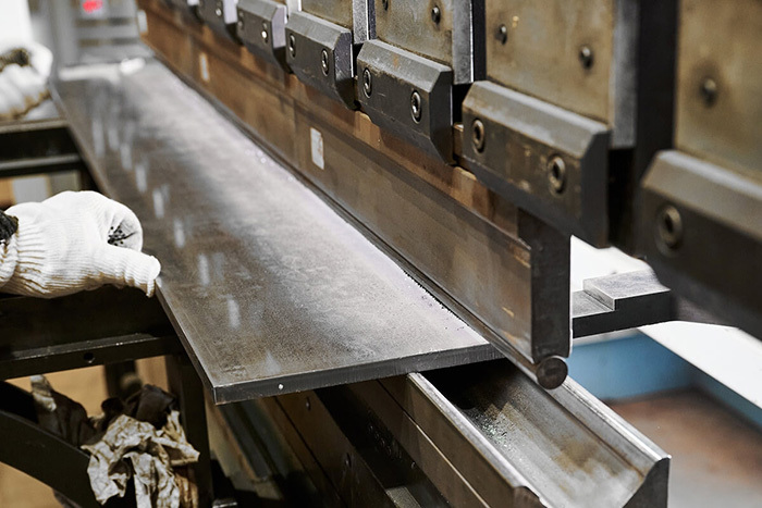 Close-up of a sheet metal bending machine in operation, with a worker’s gloved hands guiding the metal.