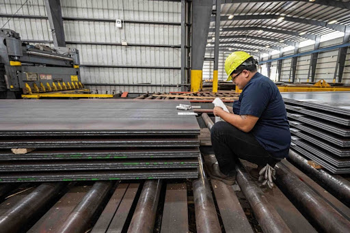 Worker inspecting stacks of steel sheets in an industrial facility.